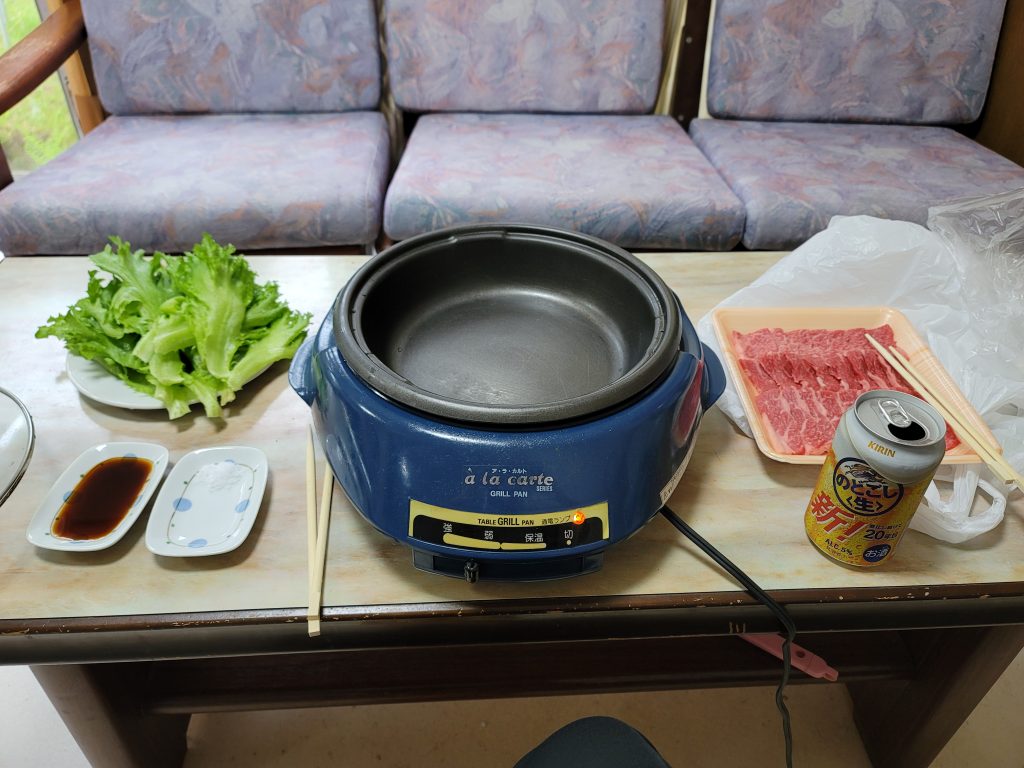 ホットプレートに焼肉、テーブルにレタスとビールが並ぶ旅の自炊ごはんの様子