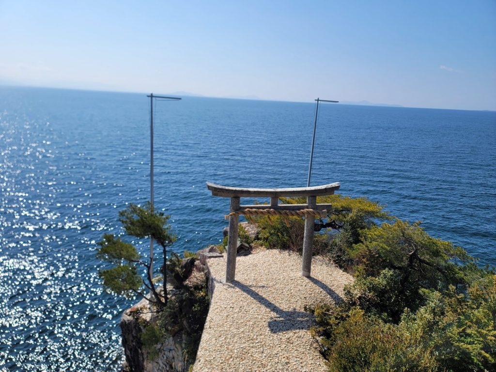 竹生島の竜神拝所で行われるかわらけ投げの様子。輝く琵琶湖を背景にした神聖な光景。