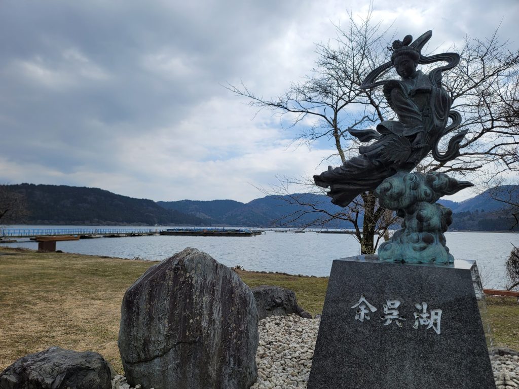余呉湖の天女の像と背後に写る静かな湖面。