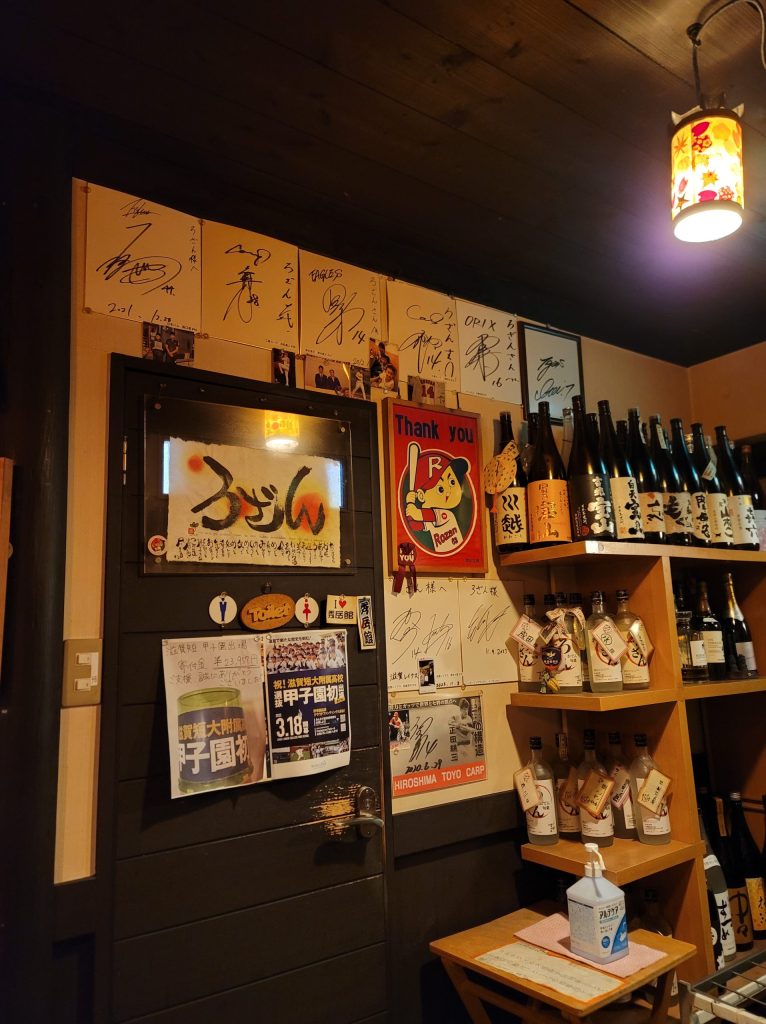 たくさんの焼酎やお酒が並ぶ棚の横に、野球選手のサインが飾られた店内の様子。