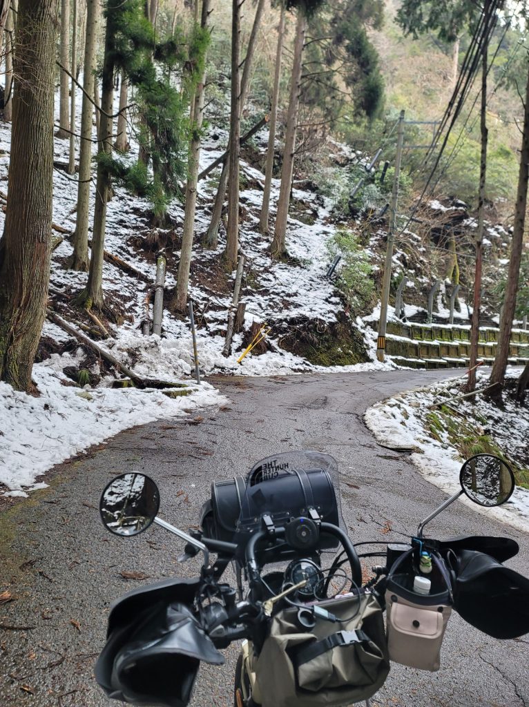 旧花背峠に向かう舗装林道の両側が雪に覆われた杉林、ハンターカブが手前に写る景色
