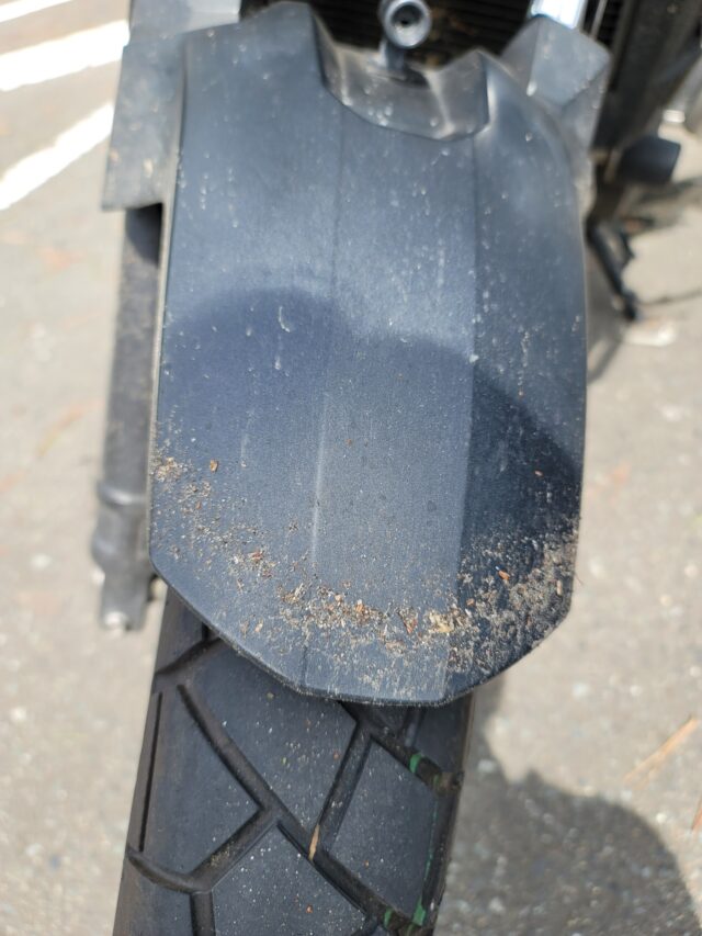 バイクがあれた道を走って泥だらけ