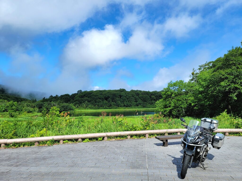 八幡平大沼の湖畔でバイクと記念撮影。空の青と湖の深い緑が美しく、岩手ツーリングで人気の絶景ポイント。