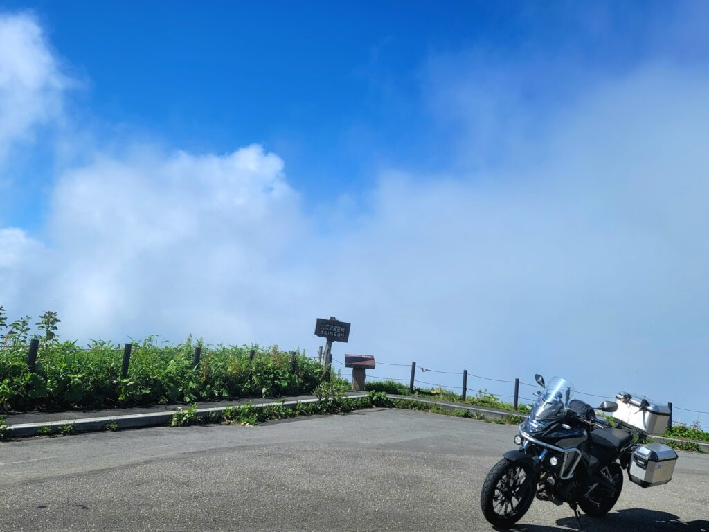 八幡平大深沢展望台での記念撮影。白い雲に覆われた空と青空のコントラストを背景に、バイクが映えるツーリングショット。