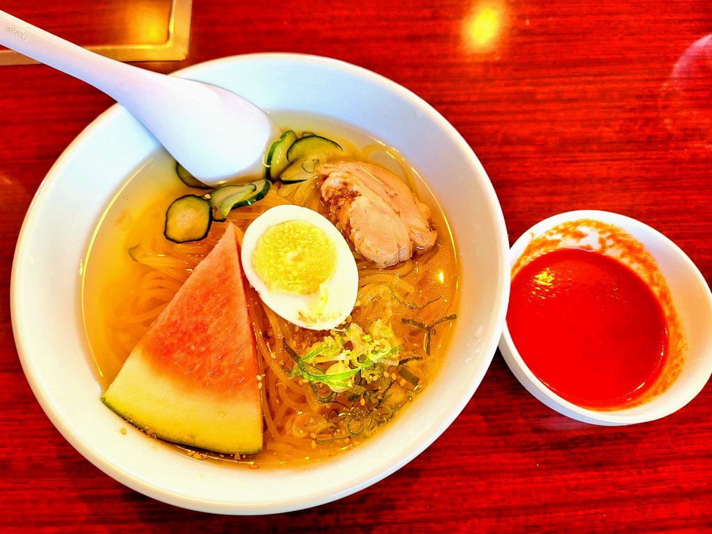 透き通ったスープにスイカ、キュウリ、ネギ、チャーシューがのった冷麺。別皿で辛みダレが添えられている