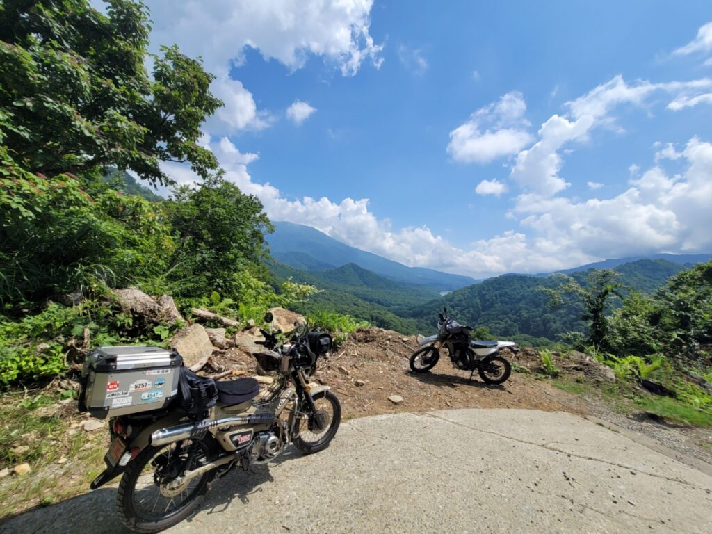 妙高小谷線、林道の絶景ポイントでハンターカブを停め、遠くの山々を背景に撮影した写真。先客のライダーもいる様子。