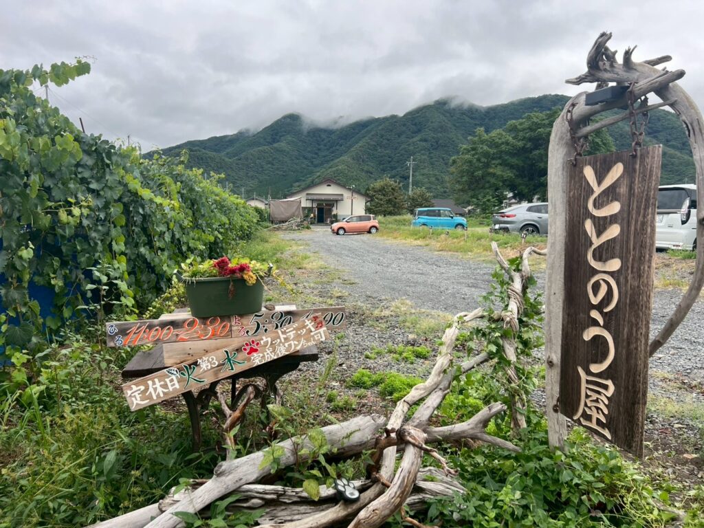長野・ブドウ畑に囲まれた自然豊かな場所に建つ「ととのうや」の外観。広々とした駐車場と家屋が見える。バイクも車も安心して停められる広い駐車場。