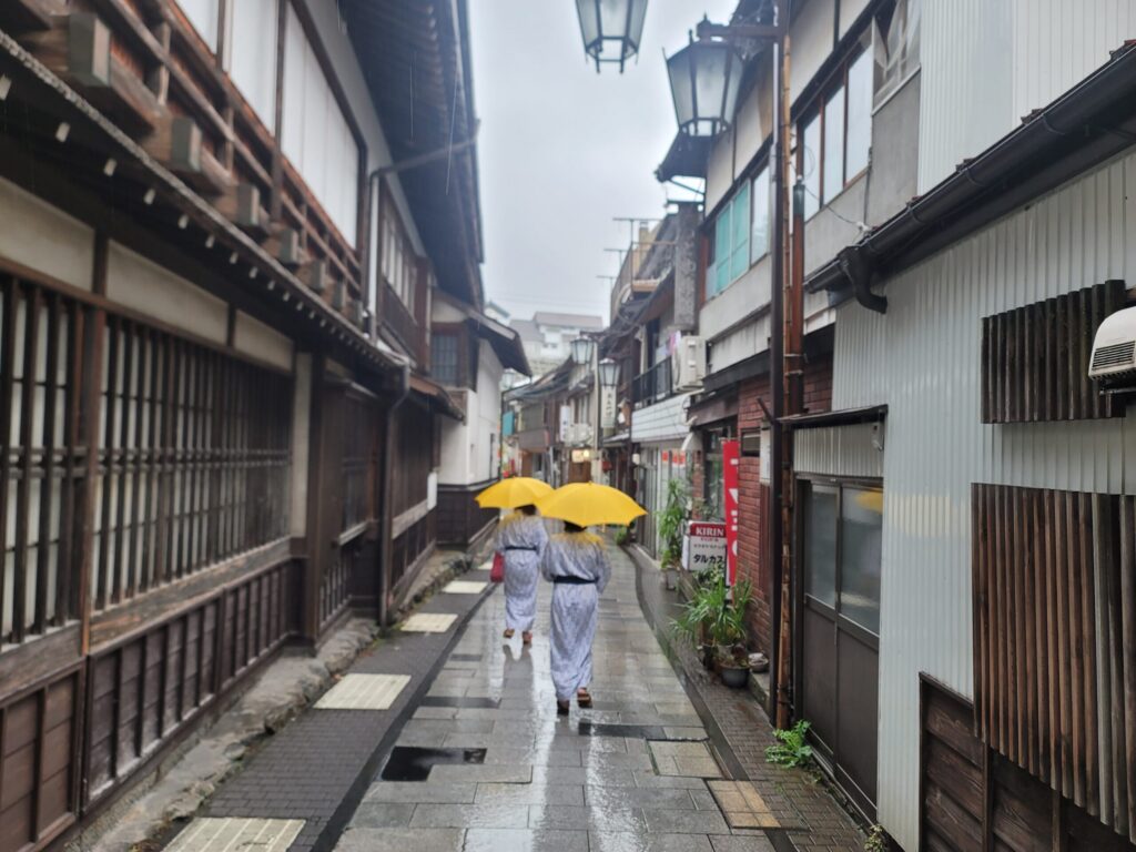 長野・渋温泉街を浴衣姿で黄色い傘をさして歩く女性グループの後ろ姿。普段はバイク女子の主の浴衣姿がまぶしい感じの写真。