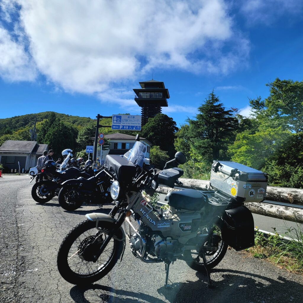 高野龍神スカイラインの休憩スポット「護摩山スカイタワー」を背後に、手前にハンターカブを写した写真。タワーの高さとバイク旅の雰囲気が伝わる。