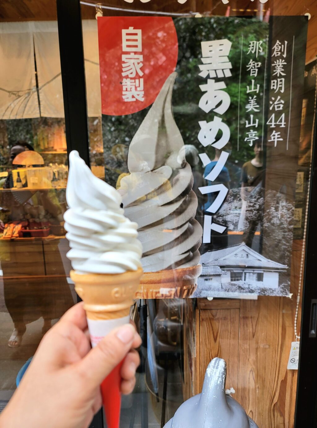 那智の滝、美山亭の黒飴ソフトクリームを手に持ち、看板前で撮影した写真。和歌山名物の黒飴スイーツ。