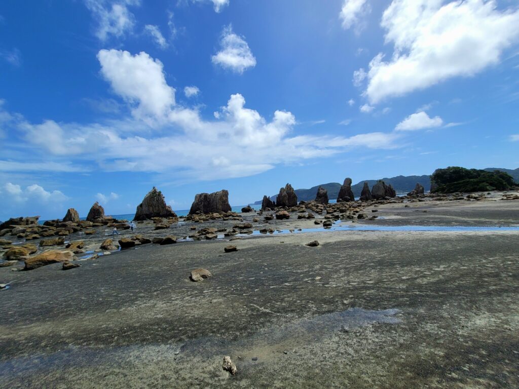 昼間の橋杭岩の写真。砂浜と奇岩、青空が広がる自然の絶景

