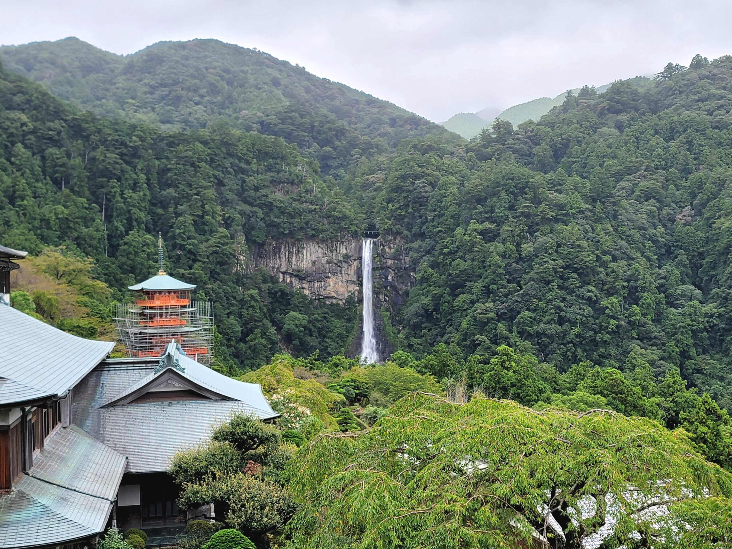 那智大社境内から見た三重塔と迫力ある那智の滝。青空の下で滝の水しぶきが輝く風景。