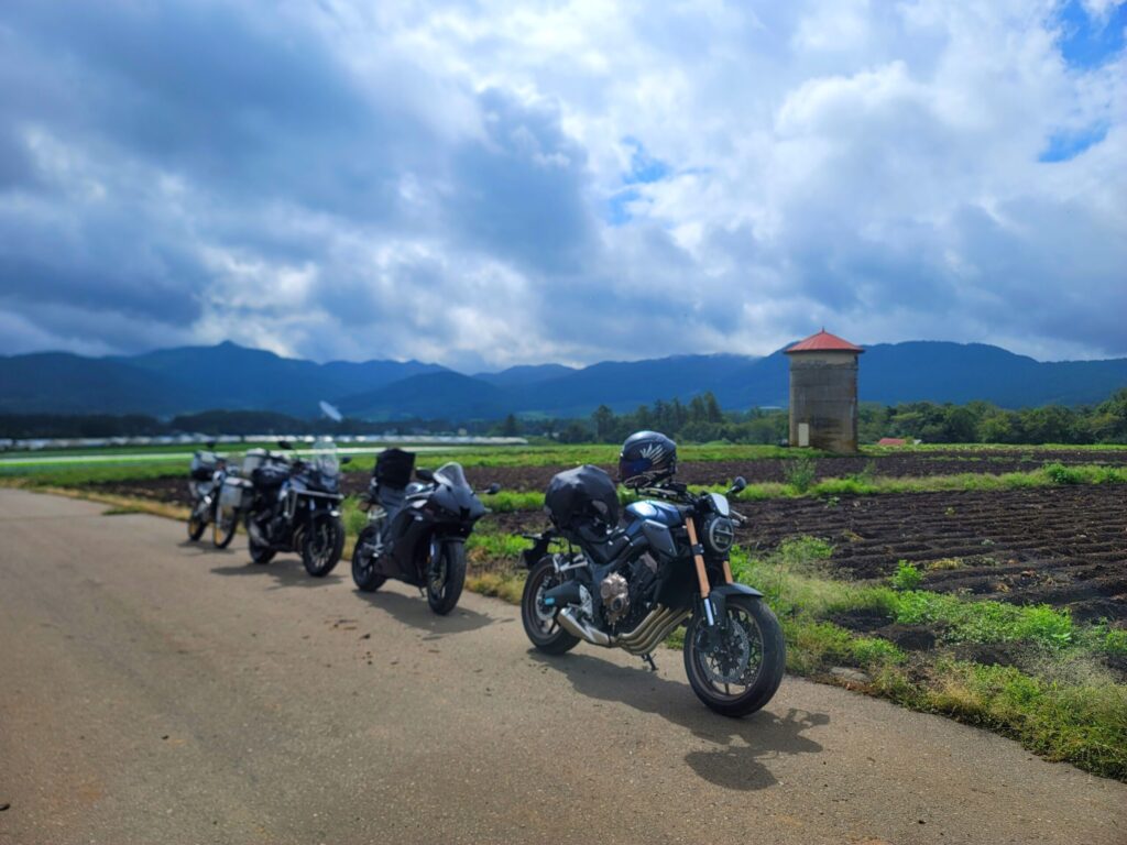 長野・野辺山天文台遠景の電波塔とサイロ、青空と畑の中でバイクを停めた風景。野辺山の絶景写真を撮る撮影スポット。