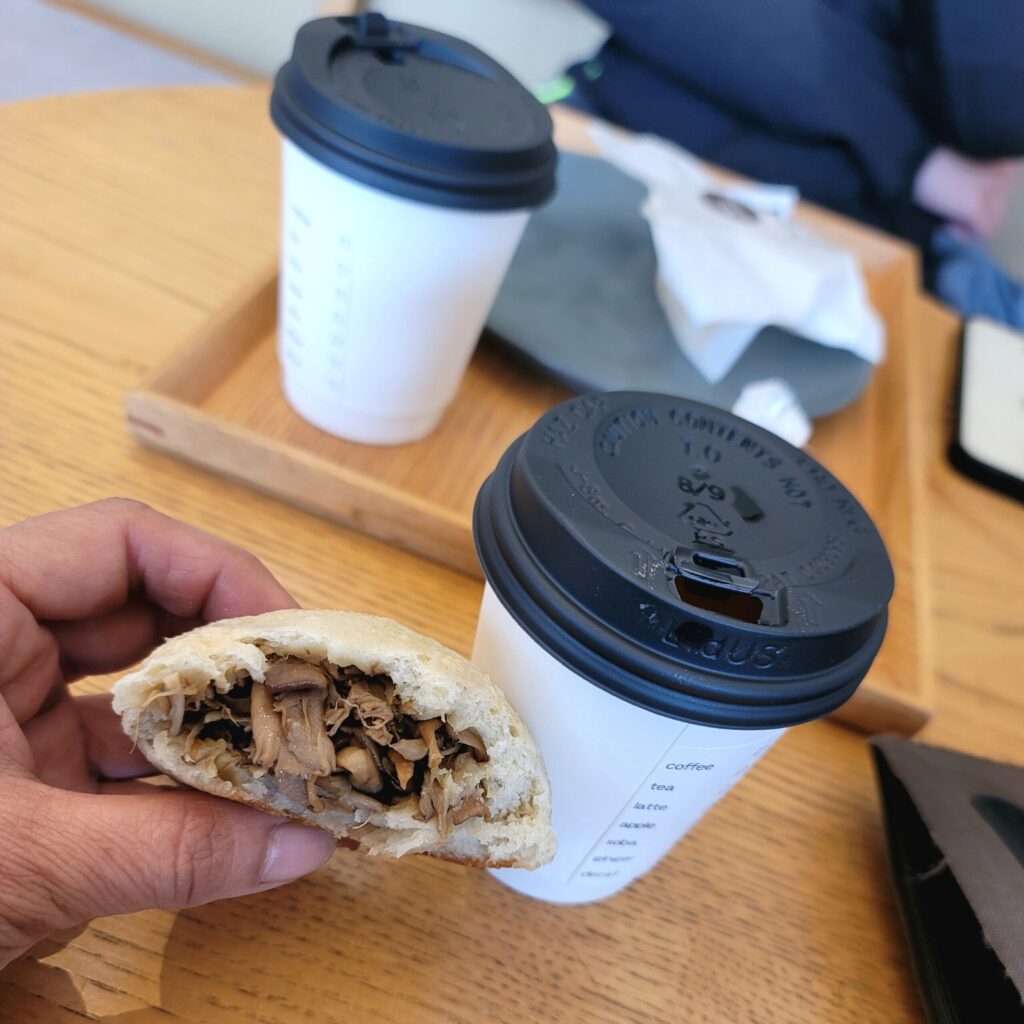 長野・川中島の焼きたてのマイタケおやきを半分に割り、香ばしい皮の中からきのこの具材を見せる様子。しっとりした生地に、香り豊かなマイタケの風味が広がる。