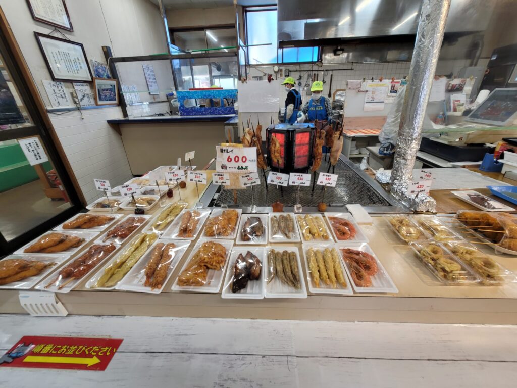 道の駅鳥海ふらっとの売店に並ぶ魚のフライ、煮魚、焼き魚などの惣菜の写真