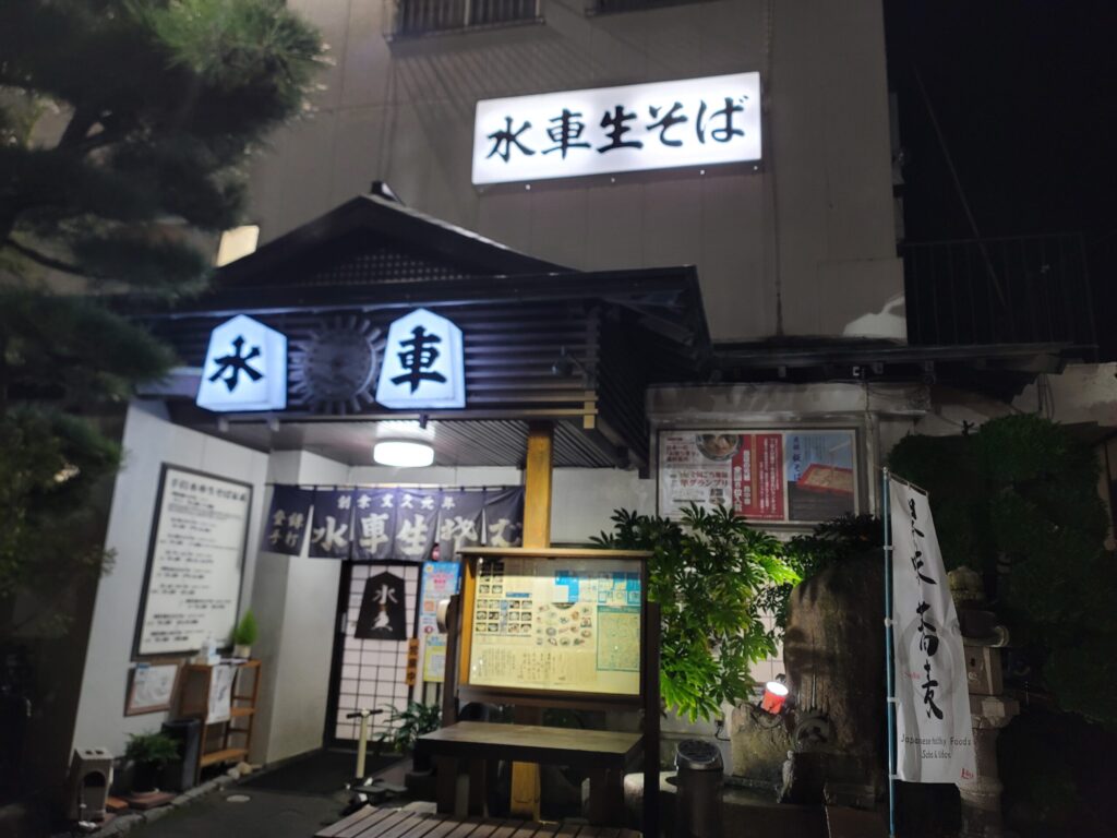 山形市の老舗そば店「水車生蕎麦」の正面外観写真。店先には看板とのれんがかかっている