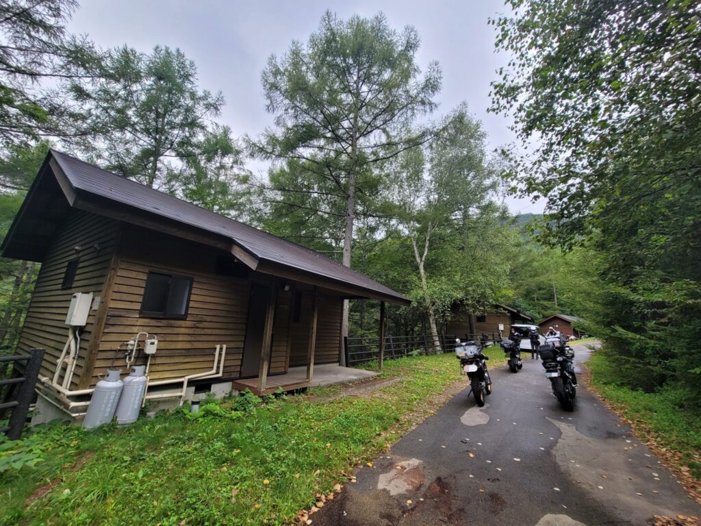 長野・立原高原ログハウス前で出発準備中の女子ライダーとバイクの後ろ姿