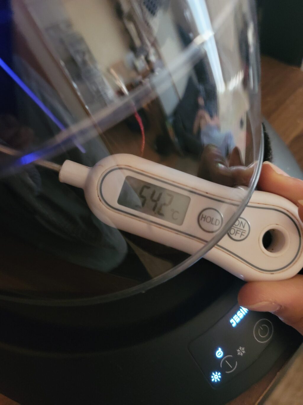 JESIMIAKヘルメット消臭乾燥機A2Sを温風モードに設定し、吹き出し口の温度を温度計で測っている写真。
耳元スピーカー部分の温度は約55℃を記録。