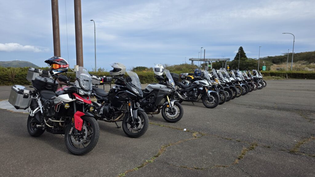 『BIKE PARADISE』の看板の下に並ぶアドベンチャーバイクの列。丘陵の緑を背景に