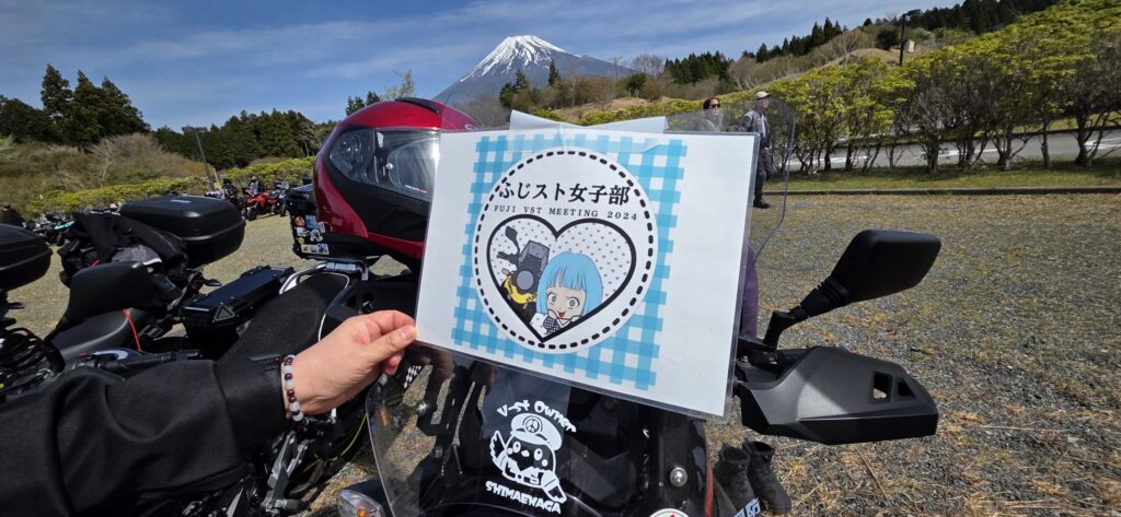 V-STROM女子部の案内版を並んだ黄色のV-STROMの前で持っている様子