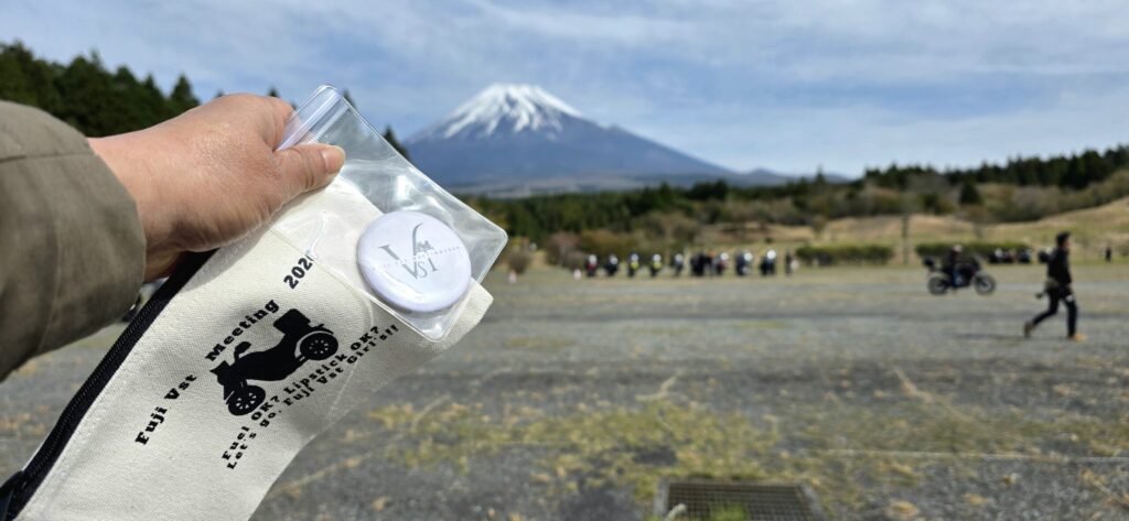 V-STROM女子に特別に配られたポーチと鏡のノベルティグッズを富士山を背景に持っている様子