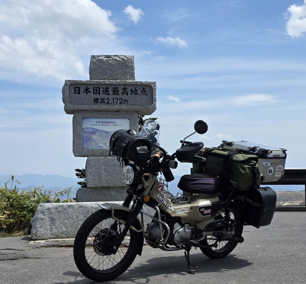 渋峠・日本国道最高地点の標識とハンターカブが写る風景