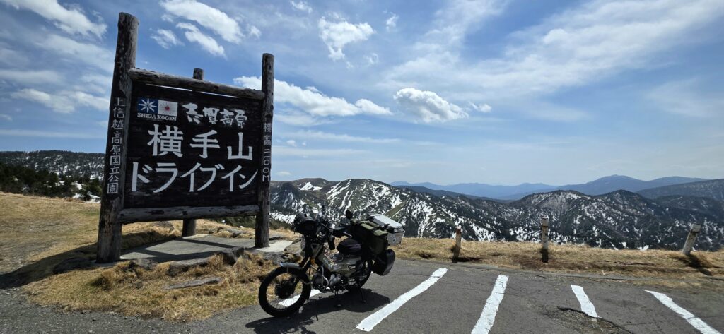 長野県渋峠横手山ドライブインの看板の前でハンターカブと残雪の山の景色