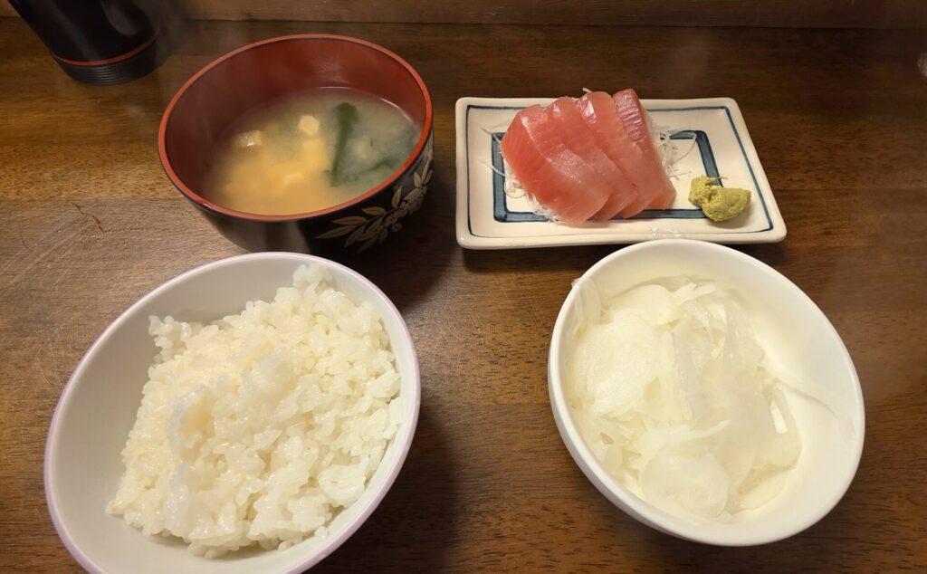 静岡県由比漁港近くの「大衆食堂おふくろ亭」ごはん、みそしる、お刺身、玉ねぎスライスがテーブルに乗っている様子