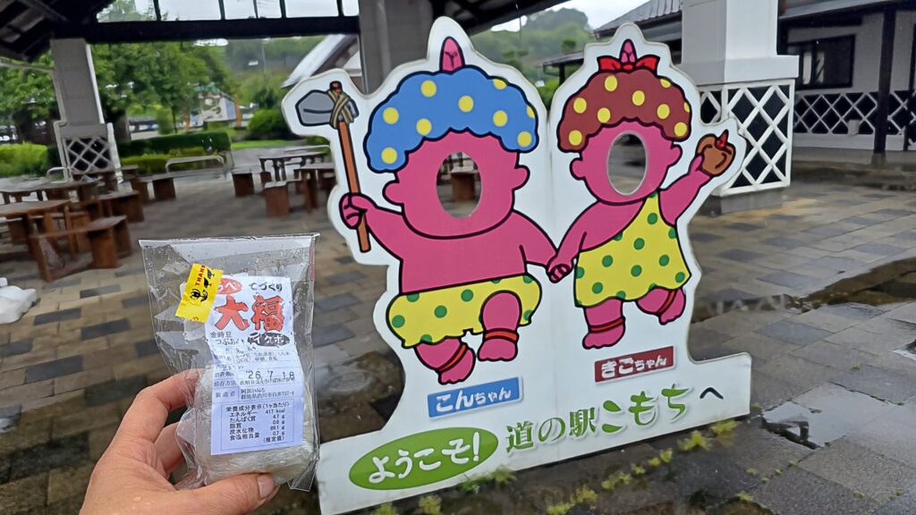 群馬・道の駅こもちのこんにゃくの妖精の前で大福を持っている様子